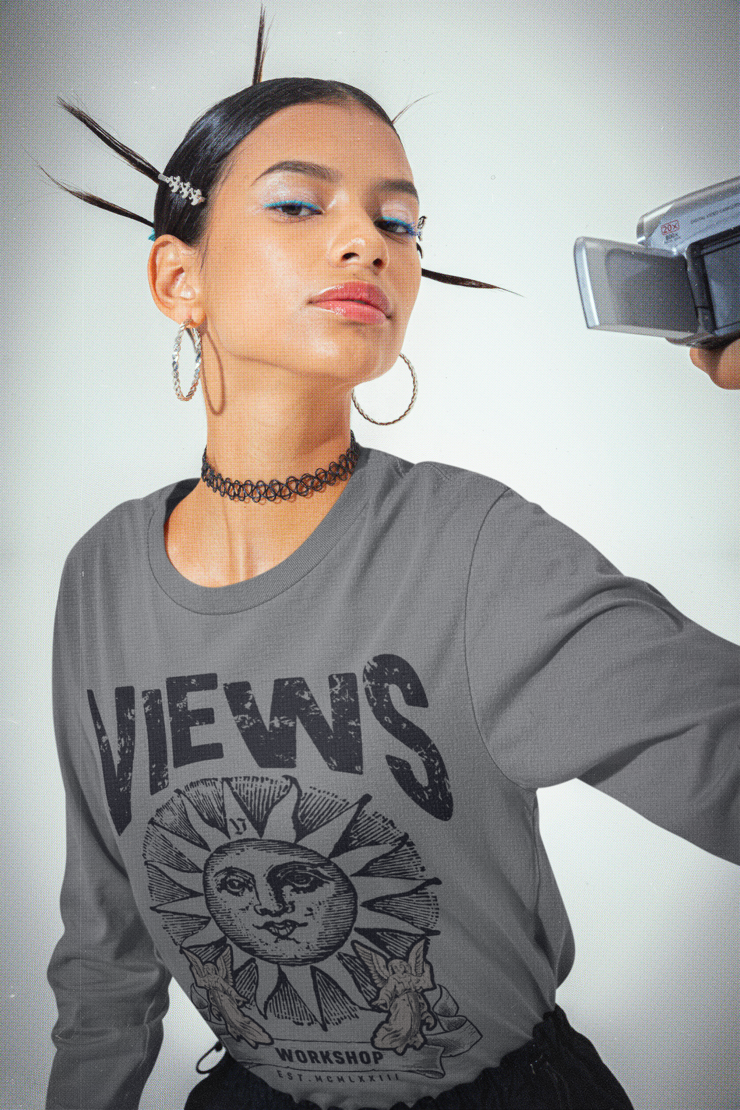 Person wearing a gray 'VIEWS' shirt with a sun design, holding a camera.