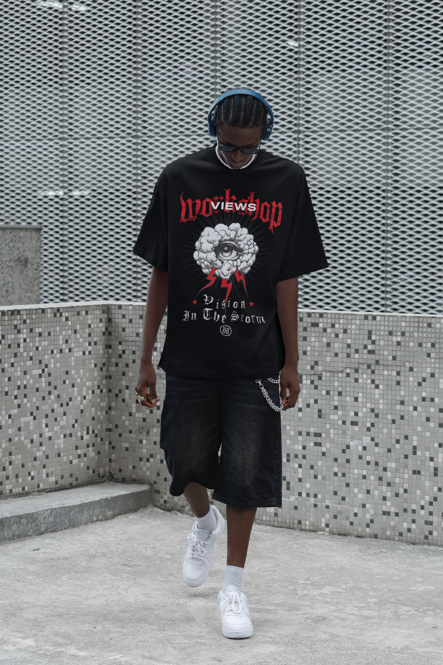 Person wearing a black Tee with graphic design and text, standing against a textured wall.
