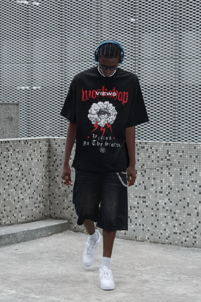 Person wearing a black Tee with graphic design and text, standing against a textured wall.